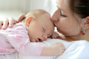 Close up of young mother holding her cute baby daughter lying on her, sleeping, kissing her